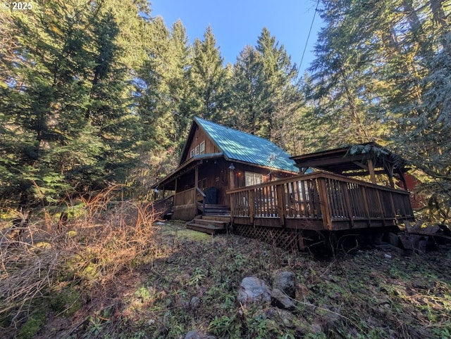 exterior space with a deck, metal roof, and a view of trees