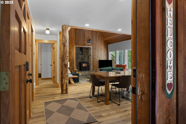 dining room with light wood-type flooring, vaulted ceiling, wooden walls, and recessed lighting