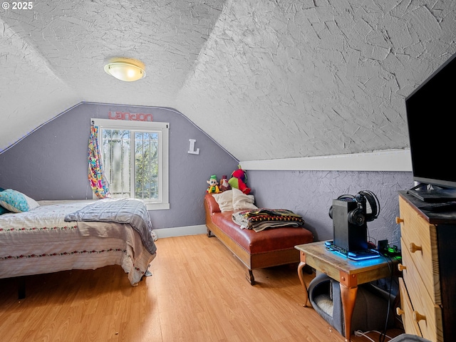 bedroom featuring baseboards, vaulted ceiling, wood finished floors, and a textured ceiling