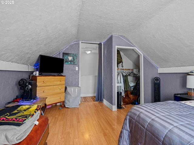 bedroom featuring vaulted ceiling, wood finished floors, a textured ceiling, and a closet
