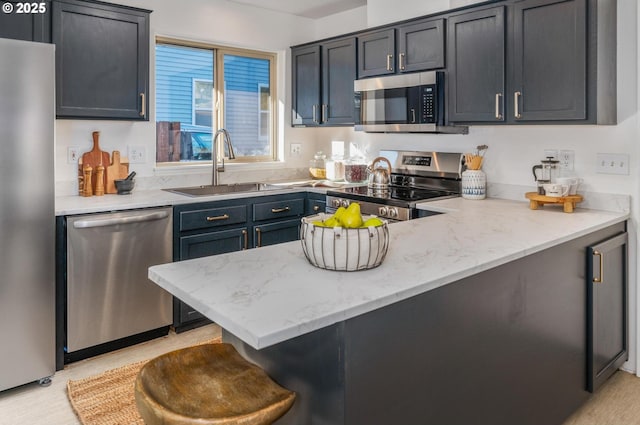 kitchen featuring light stone counters, a breakfast bar, a peninsula, stainless steel appliances, and a sink