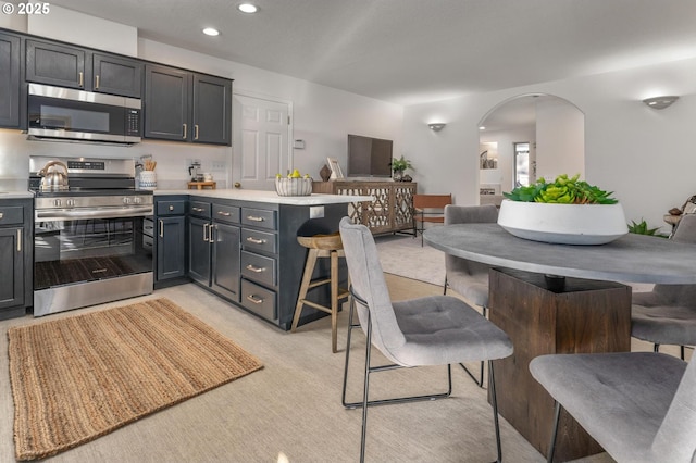 kitchen with arched walkways, a breakfast bar, appliances with stainless steel finishes, open floor plan, and a peninsula