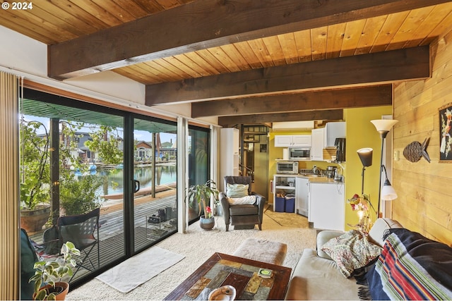 carpeted living room featuring beam ceiling, a water view, wood ceiling, and wood walls