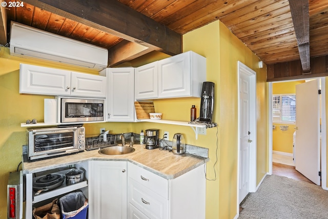 kitchen featuring white cabinets, beam ceiling, stainless steel microwave, and sink