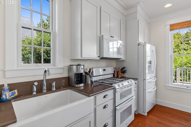 kitchen featuring white appliances, a sink, dark countertops, wood finished floors, and white cabinetry