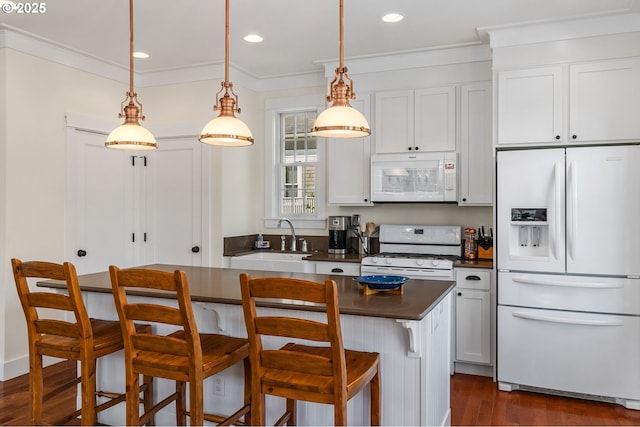 kitchen featuring white appliances, a sink, dark wood-type flooring, ornamental molding, and a breakfast bar area