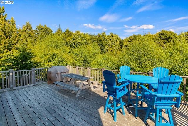 wooden terrace featuring outdoor dining area, area for grilling, and a forest view