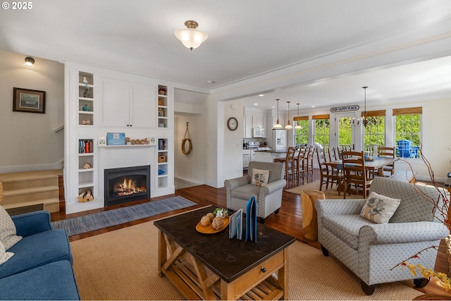 living area featuring built in shelves, wood finished floors, a fireplace with flush hearth, and baseboards