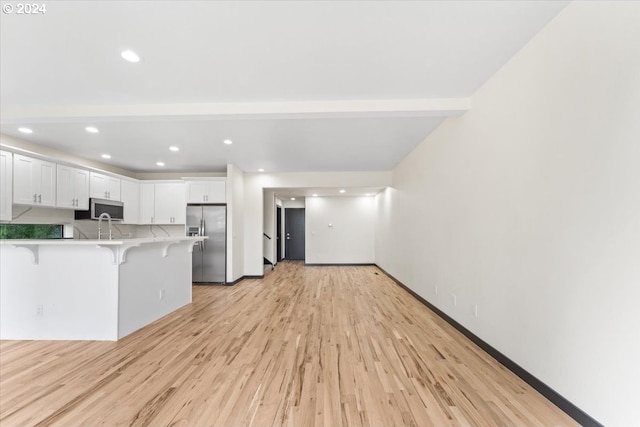 kitchen with kitchen peninsula, a kitchen breakfast bar, stainless steel appliances, light hardwood / wood-style flooring, and white cabinetry