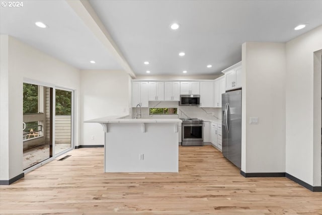 kitchen with appliances with stainless steel finishes, light wood-type flooring, a breakfast bar, white cabinetry, and an island with sink