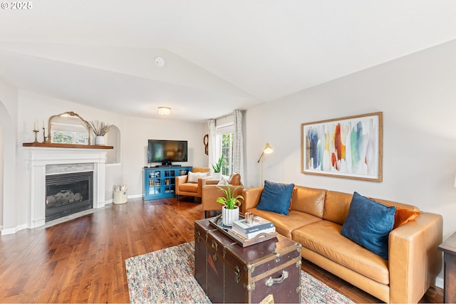 living area featuring baseboards, vaulted ceiling, wood finished floors, and a glass covered fireplace