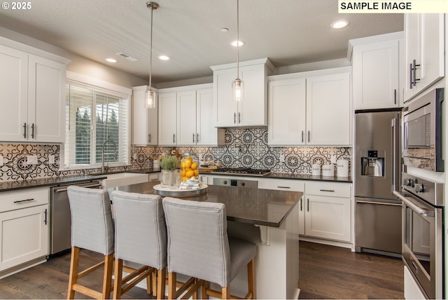 kitchen featuring stainless steel appliances, dark countertops, visible vents, and a kitchen breakfast bar