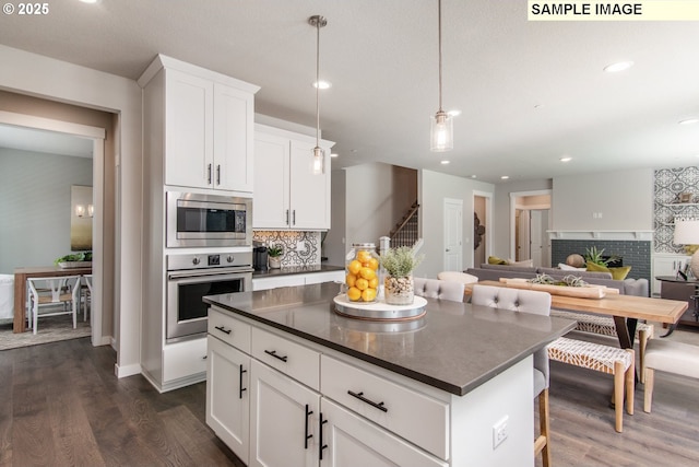 kitchen with appliances with stainless steel finishes, dark countertops, dark wood-style flooring, and a kitchen island