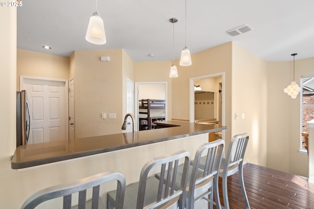 kitchen with visible vents, freestanding refrigerator, a sink, a kitchen bar, and decorative light fixtures