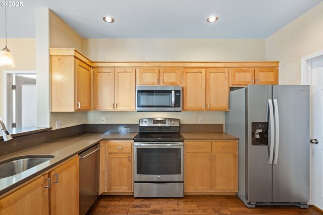 kitchen with dark wood-style flooring, pendant lighting, light brown cabinetry, a sink, and stainless steel appliances