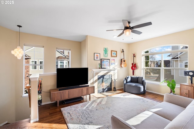 living area with a glass covered fireplace, a ceiling fan, baseboards, and wood finished floors