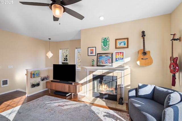 living area featuring ceiling fan, a fireplace, baseboards, and wood finished floors