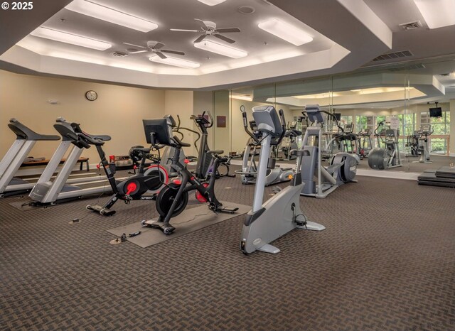 exercise room featuring visible vents, a ceiling fan, a tray ceiling, and carpet flooring