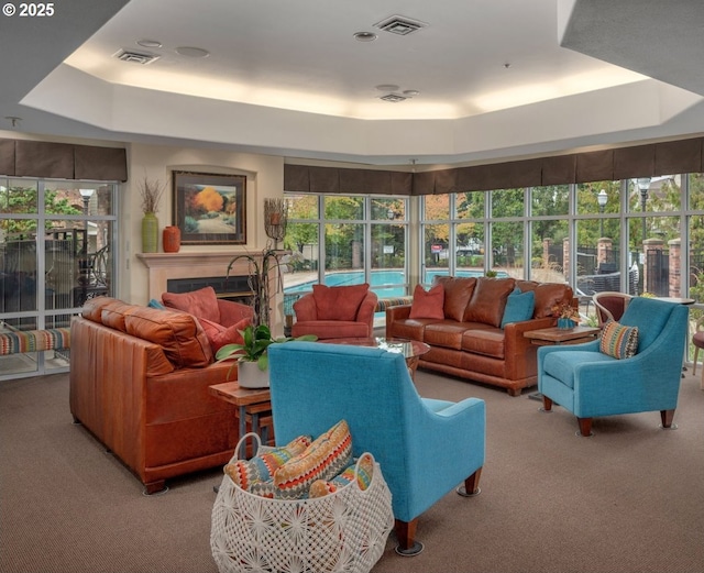 carpeted living room featuring a tray ceiling, a fireplace, and visible vents