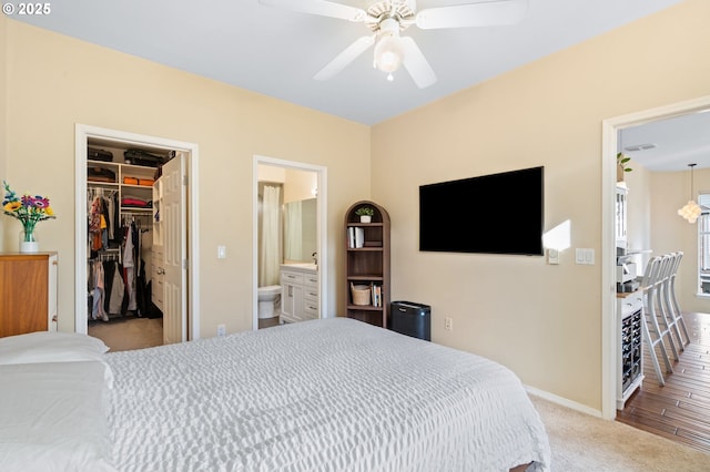 carpeted bedroom with a walk in closet, baseboards, ensuite bathroom, a closet, and a ceiling fan