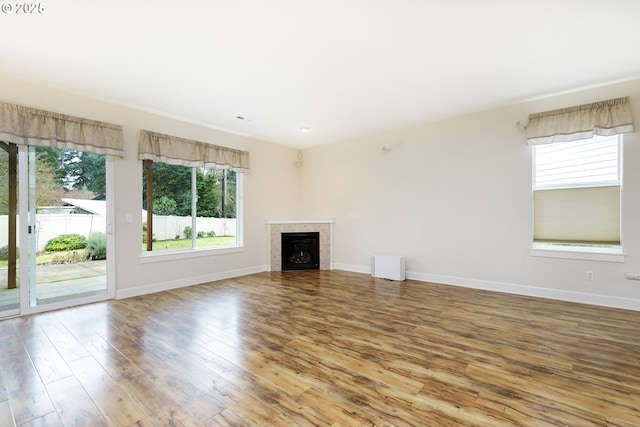 unfurnished living room featuring wood-type flooring, a tiled fireplace, and a wealth of natural light