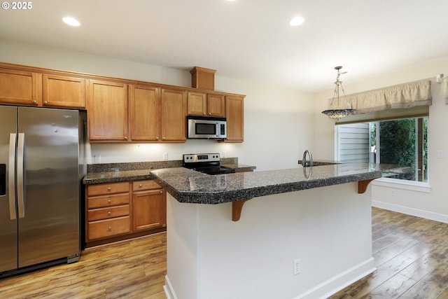 kitchen featuring stainless steel appliances, hanging light fixtures, light wood-type flooring, a breakfast bar, and a center island with sink