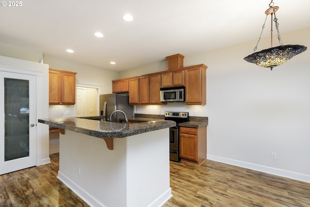 kitchen with a kitchen bar, appliances with stainless steel finishes, wood-type flooring, sink, and a center island with sink