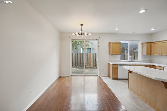 kitchen featuring pendant lighting, light hardwood / wood-style flooring, dishwasher, tile countertops, and a chandelier