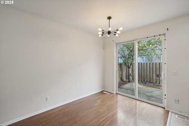 spare room with an inviting chandelier and hardwood / wood-style flooring