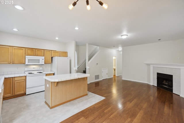 kitchen featuring a kitchen island, wood-type flooring, a tiled fireplace, tile counters, and white appliances