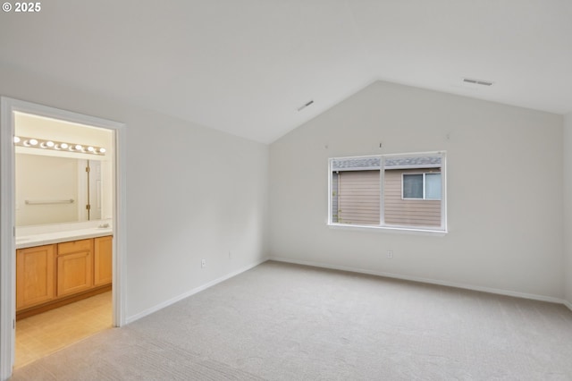 interior space featuring lofted ceiling, connected bathroom, and light colored carpet