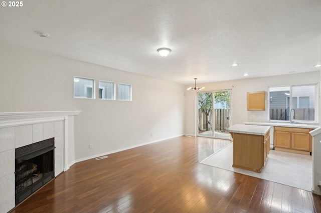 kitchen with a tiled fireplace, decorative light fixtures, a center island, and light hardwood / wood-style flooring