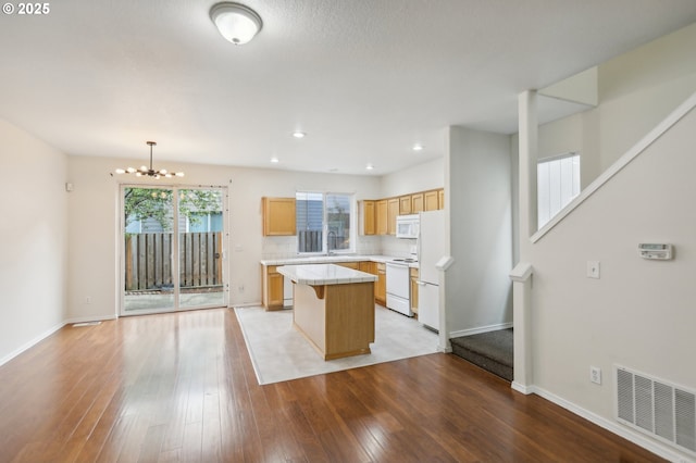 kitchen featuring a chandelier, a center island, hanging light fixtures, light wood-type flooring, and white appliances