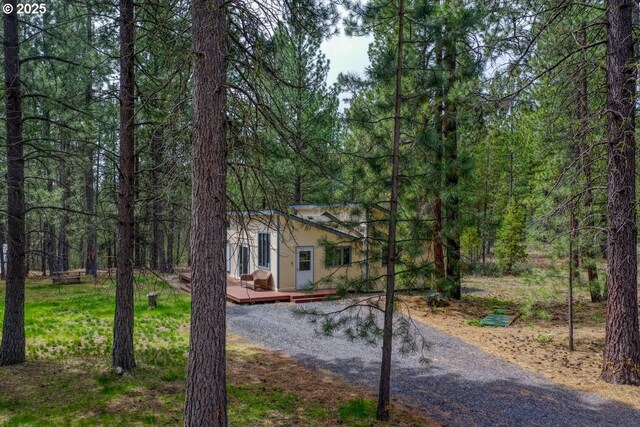 16811 Covina Rd, Bend, OR 97707 - view of front of home with a wooden deck, a wooded view, gravel driveway, and stucco siding