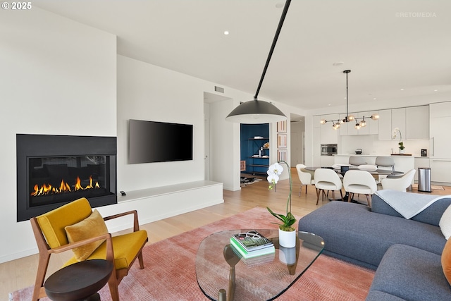 living room with light wood-type flooring, a glass covered fireplace, a chandelier, and recessed lighting