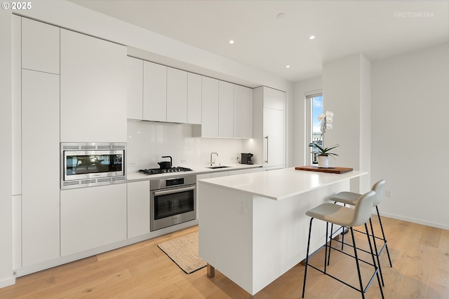 kitchen with stainless steel appliances, a sink, a kitchen bar, modern cabinets, and light wood-type flooring