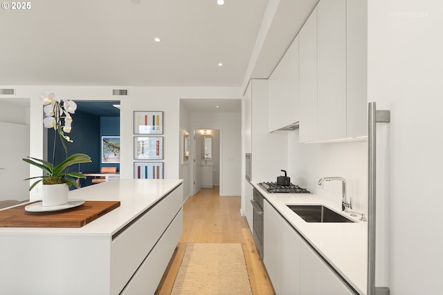 kitchen with a sink, modern cabinets, white cabinets, light wood-style floors, and light countertops