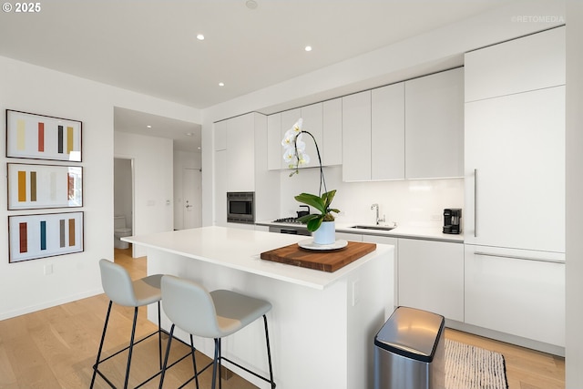 kitchen featuring a sink, white cabinets, a breakfast bar, a kitchen island, and recessed lighting