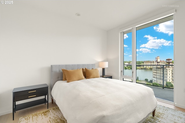 bedroom with access to exterior, a water view, wood finished floors, and baseboards