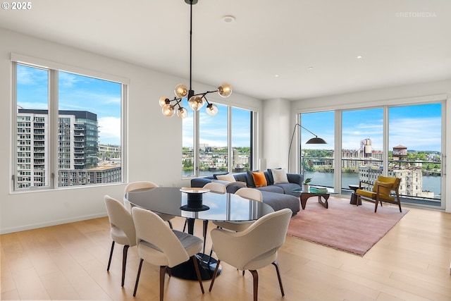 dining space featuring light wood-style floors, a chandelier, a water view, a view of city, and baseboards