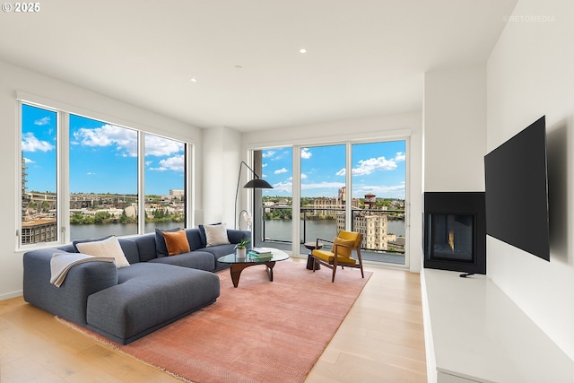 living room featuring a water view, light wood-type flooring, recessed lighting, and a glass covered fireplace