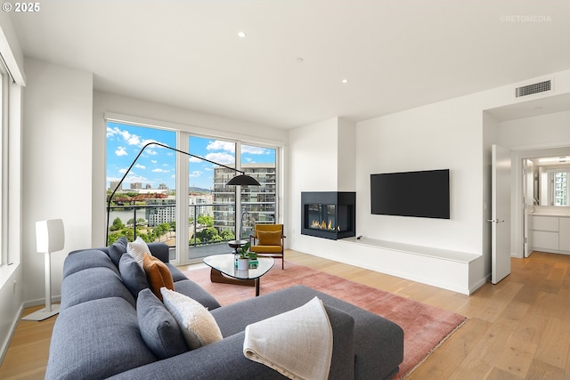 living area with light wood-style floors, a glass covered fireplace, and recessed lighting
