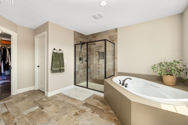 bathroom featuring a spacious closet, stone finish floor, baseboards, a garden tub, and a stall shower