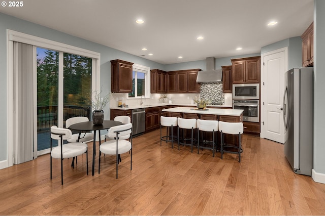 kitchen featuring wall chimney exhaust hood, a center island, a kitchen breakfast bar, stainless steel appliances, and backsplash