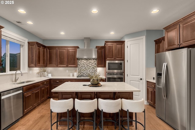 kitchen with stainless steel appliances, a center island, sink, and wall chimney range hood