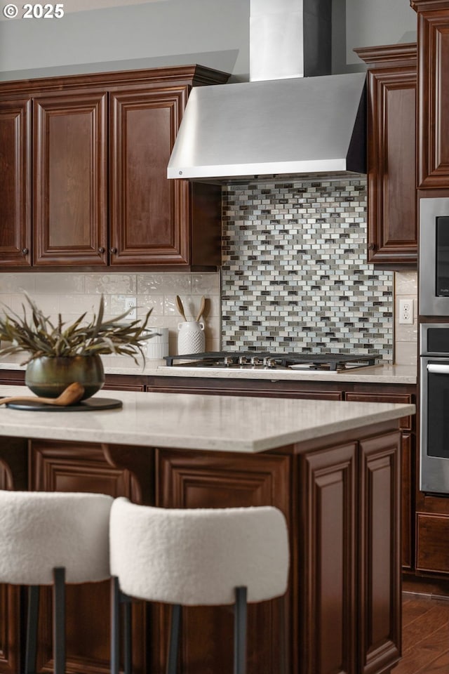 kitchen featuring a breakfast bar, appliances with stainless steel finishes, dark hardwood / wood-style floors, decorative backsplash, and wall chimney exhaust hood