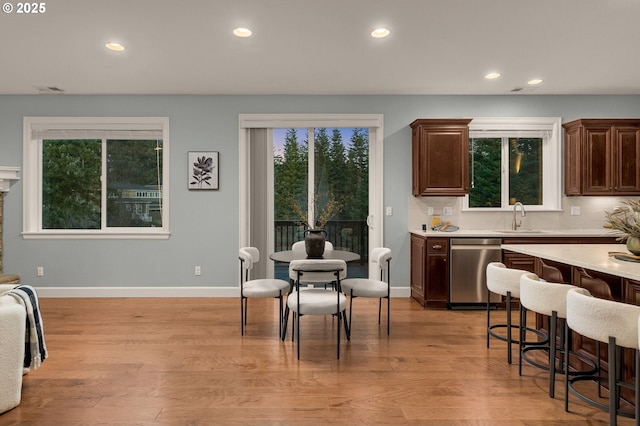 kitchen with tasteful backsplash, dishwasher, sink, a kitchen bar, and light wood-type flooring