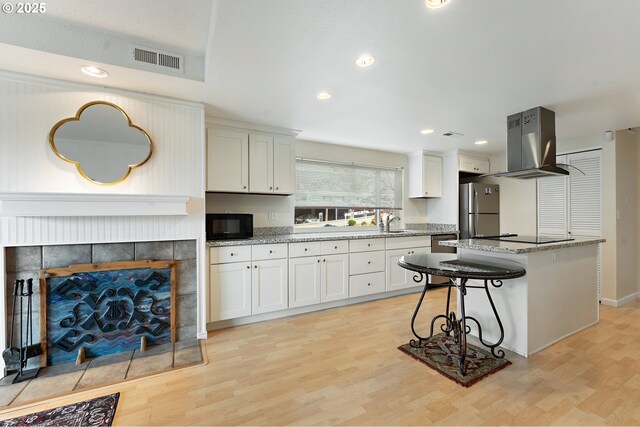 kitchen with light wood-style floors, visible vents, island exhaust hood, and black appliances