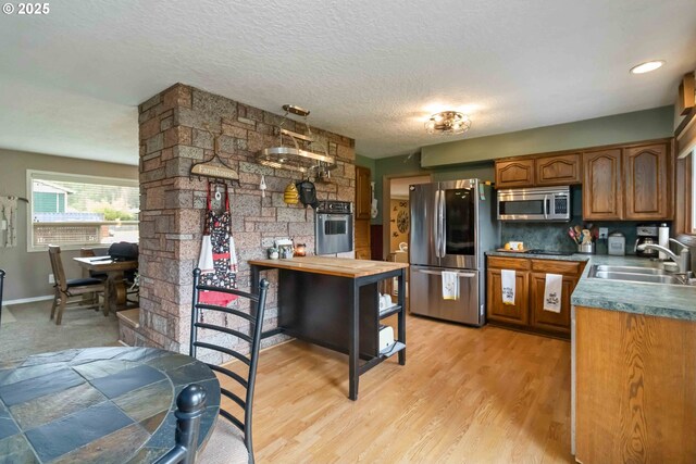 772 Elochoman Valley Rd, Cathlamet, WA 98612 - kitchen featuring appliances with stainless steel finishes, a sink, brown cabinetry, light wood finished floors, and a textured ceiling