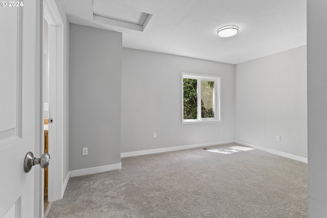 carpeted empty room with baseboards and attic access